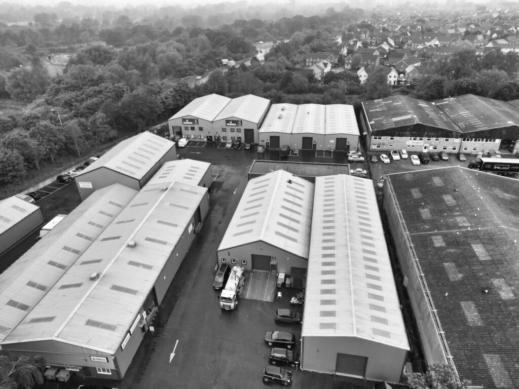 Black and white aerial view of industrial warehouses surrounded by greenery in Essex, UK.