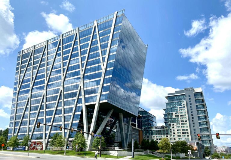 Tall modern office building with glass facade in an urban setting under a clear blue sky.