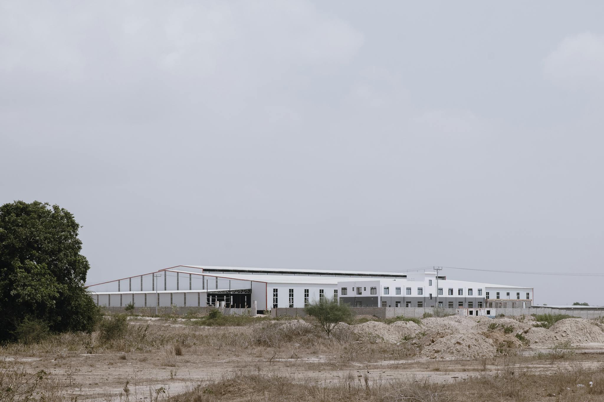 A large industrial building set in an empty rural landscape under a cloudy sky.